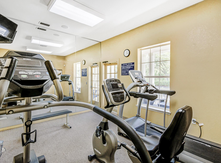Fitness center equipped with multiple exercise machines, dumbbell free weights and mirror wall